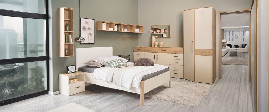 Schlafzimmer mit Bett, Kommode und weiteren Schränken in Artisan Eiche Nachbildung und einer sandfarbigen Front