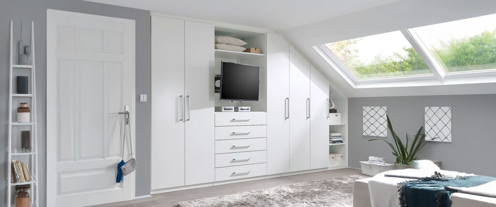 Dachzimmer mit weißen Möbeln. Auf der rechten Seite sind die Möbel passend zur Dachschräge abgeschrägt