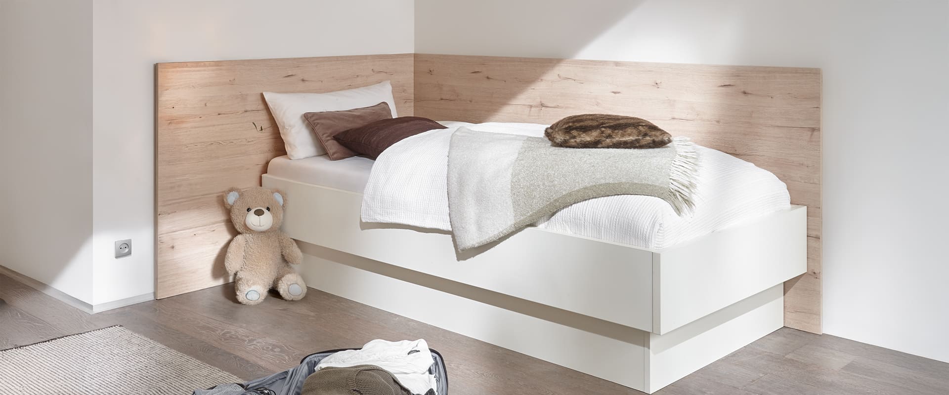 Paneelrückwand über Ecke in Eiche San Remo Nachbildung. Ein Schutz vor Verschmutzung der Wand. Davor steht ein weißes zweitloses Studio Bett.